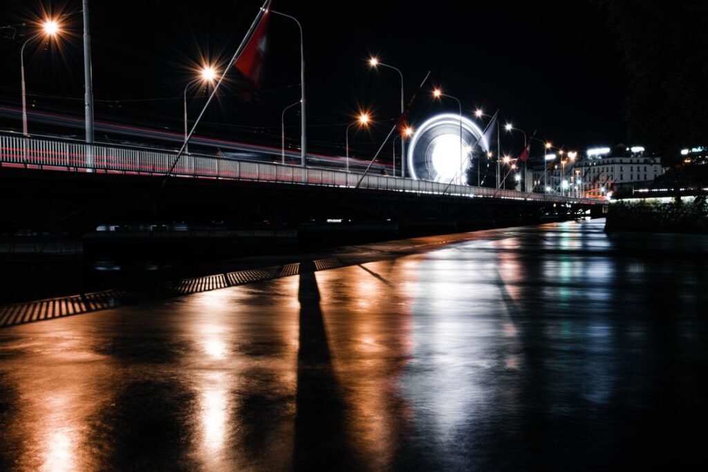 Vue nocturne de Genève avec pont illuminé et grande roue reflétés sur le pavé